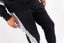 Black sweatpants with three white stripes down the side, worn by a model against a plain white background. By Fresh N Fitted 
