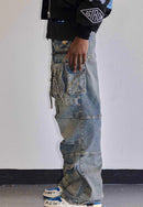 A person shown from the chest down wearing heavily distressed light-wash blue cargo jeans with multiple pockets, a black jacket with a sleeve patch, and white sneakers against a plain indoor wall.