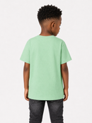 A child viewed from the back wearing a light mint green short-sleeve t-shirt and dark gray jeans, standing against a plain white studio background.