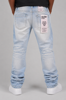 Back view of a person wearing light-wash blue jeans with a large white patch on the back pocket and white sneakers, photographed against a light gray studio background. By Fresh N Fitted.