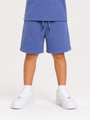 A child wearing blue speckled shorts with a drawstring and a matching blue top, paired with white sneakers, shown from the waist down against a light gray studio background.