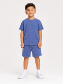 A young boy modeling a matching blue heathered t-shirt and shorts set with white sneakers, standing against a plain white studio background.