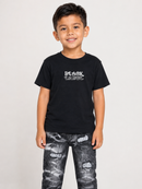 A young boy smiling and wearing a black crewneck t-shirt with a white graphic text print on the chest that reads 'BLACK TANKS', paired with distressed black and gray jeans, against a plain light gray background.