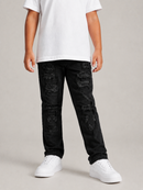 A child wearing black heavily distressed denim jeans with ripped details, styled with a white t-shirt and white sneakers against a neutral studio background.