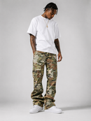 A man modeling a pair of camouflage cargo pants with a white t-shirt and white sneakers, standing against a light gray studio background.