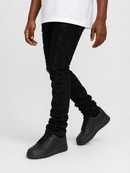 A person wearing black distressed skinny jeans with frayed details, styled with a white t-shirt and black low-top sneakers against a light gray studio background.