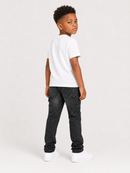 A young boy standing in profile wearing a white short-sleeve t-shirt, dark gray speckled jeans, and white sneakers against a light gray studio background.