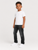 A young boy modeling a white crewneck t-shirt, dark gray distressed skinny jeans, and white sneakers, standing against a light gray studio background.