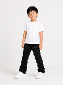 A young boy modeling a white crewneck t-shirt and black distressed denim jeans with white sneakers, standing against a plain white studio background.