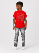 A child model shown from the back wearing a bright red t-shirt with a large tonal red graphic on the back, paired with gray and white marbled jeans and white sneakers, against a light gray studio background.