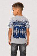 A child model shown from the back wearing a light gray heather t-shirt with a large blue and navy 'GRIZZLY 00' graphic with lightning details, paired with dark gray jeans, against a light gray studio background.