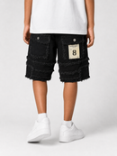 A person shown from the waist down wearing black frayed denim shorts with multiple patch pockets and a cream paper label on the back pocket, paired with a white t-shirt and white sneakers against a light gray studio background.