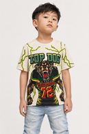 A young boy wearing a cream-colored graphic t-shirt with a green and black bear design and the text 'TOP DOG' and 'STANDOUT 72', paired with light blue jeans, against a plain light gray background.