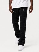 A person wearing black patchwork frayed denim jeans with a white t-shirt and white sneakers, shown from the waist down against a light gray studio background.