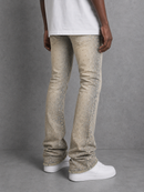 A person shown from the waist down wearing light beige denim jeans with a subtle speckled texture, a white t-shirt, and white sneakers against a gray studio background.