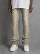 A person wearing light beige distressed jeans with a subtle dotted pattern, styled with a white t-shirt and white sneakers against a gray concrete wall.