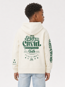 A child model shown from the back wearing an off-white hooded sweatshirt with green graphic text and illustrations on the back and sleeve, paired with light blue jeans against a plain light gray studio background.