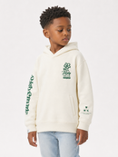 A young boy wearing a cream-colored hoodie with green graphic prints on the chest, sleeve, and cuff, paired with light blue jeans, photographed against a plain white studio background.