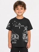 A young boy with curly brown hair smiling, wearing a black short-sleeve graphic t-shirt with white text and illustrations, set against a plain light gray background.