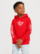 A young boy wearing a bright red hoodie with white graphic prints and light blue jeans, standing against a light gray studio background.