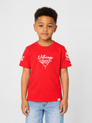 A young boy wearing a red short-sleeve t-shirt with a white graphic print on the front that reads 'Nothing GIVEN' and light wash blue jeans, standing against a light gray studio background.