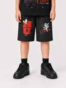 A child modeling black shorts with red and white graphic prints, paired with a black graphic t-shirt and black sneakers, against a light gray studio background.