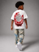A child model shown from behind wearing a white t-shirt with a large red and gray graphic print on the back, paired with distressed jeans and white sneakers, against a gray studio background. By Fresh N Fitted