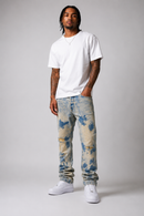 A man modeling light-wash blue and beige tie-dye jeans, a white t-shirt, and white sneakers against a neutral gray studio background. By Fresh N Fitted