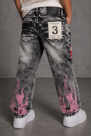 A person shown from the back wearing washed black denim jeans with bright pink flame graphics near the hems and a white patch on the back pocket, standing against a gray studio background. by Fresh N Fitted