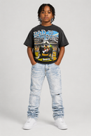 A child model wearing a black graphic t-shirt with a bulldog print and the text 'BAD TO THE BONE', paired with light-wash distressed jeans and white sneakers, standing against a light gray studio background. by Fresh N Fitted