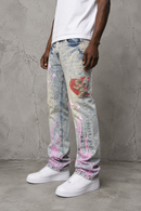 A person wearing light-tint distressed jeans with pink and red graphic, a white t-shirt, and white sneakers, standing against a textured gray concrete wall. By Fresh N Fitted.