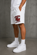 White athletic shorts with a red and black 'ATHLETIC DEPARTMENT' graphic on the left leg, worn by a model with white crew socks and white sneakers against a gray concrete wall. By Fresh N Fitted 
