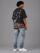 A man wearing a black graphic t-shirt with a colorful container ship design on the back, paired with light blue jeans and white sneakers, photographed from the back against a gray studio background. By Fresh N Fitted