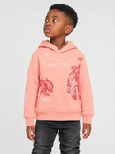 A young boy wearing a peach-pink hoodie with red and white graphic prints, paired with dark gray jeans, standing against a light gray studio background.