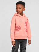 A young boy wearing a coral pink hoodie with red graphic prints and white text, paired with dark gray jeans, standing against a light gray studio background.