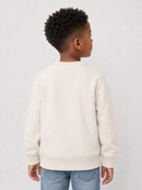 A child model shown from the back wearing a cream-colored crewneck sweatshirt and blue jeans against a plain light gray background.