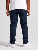 Rear view of a person wearing dark navy blue jeans, a white t-shirt, and white sneakers against a light gray studio background.