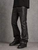 Black leather jeans with tonal embossed floral and circular patterns, worn with black sneakers against a textured gray studio background. By Fresh N Fitted