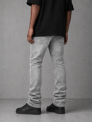 A person shown from the back wearing light gray washed skinny jeans, a black t-shirt, and black platform sneakers against a textured gray studio background.