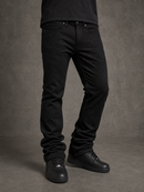 A person wearing slim-fit black jeans with black sneakers, shown from the waist down against a textured gray studio backdrop.
