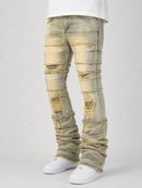Distressed light-wash denim jeans with heavy fraying, rips, and layered paneling on the legs, shown on a model wearing white sneakers against a light gray studio background.