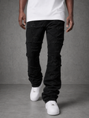 A person wearing black distressed ripped jeans with a faded wash, styled with a white t-shirt and white sneakers, standing against a gray textured studio background.