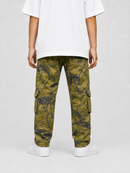 A person shown from the back wearing olive green and black camouflage cargo pants, a white t-shirt, and white sneakers against a light gray studio background.