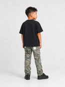 A child model shown from the back wearing a black short-sleeve t-shirt, camouflage cargo pants, and black sneakers, standing against a light gray studio background.