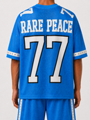 A person shown from the back wearing a bright blue jersey with large white 'RARE PEACE' lettering and the number 77 outlined in black, paired with matching blue shorts against a light gray studio background. By Fresh N Fitted.
