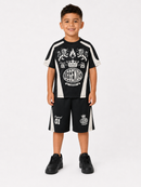 A young boy modeling a black and white athletic set consisting of a short-sleeve t-shirt and matching shorts with white graphic prints, photographed against a light gray studio background.