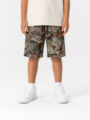 A child wearing camouflage print shorts with a beige t-shirt and white sneakers, shown from the waist down against a plain white studio background.