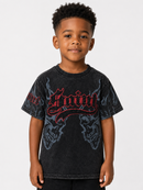 A young boy wearing a black acid-wash graphic t-shirt with red gothic lettering and skull designs, photographed against a light gray studio background.