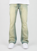 A person wearing light-wash, faded blue-green flare jeans with white sneakers, shown from the waist down against a plain light gray studio background.