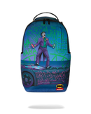 A sprayground backpack available at fresh n fitted featuring a vibrant graphic print of the Joker from Batman, standing on a car with graffiti-style text. The backpack has a black top handle, black side pockets, and a small Batman logo patch near the bottom right corner.